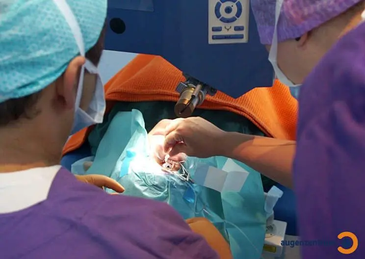 Patient liegt auf dem Rücken auf dem OP Tisch unter einer OP Lampe und bekommt Betäubungstropfen ins Auge getropft.
