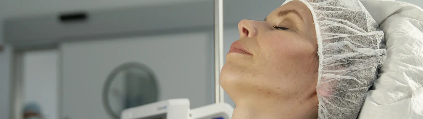 Patientin mit Haarhaube mit geschlossenen Augen bereits in Dämmerschlaf in der OP Vorbereitung